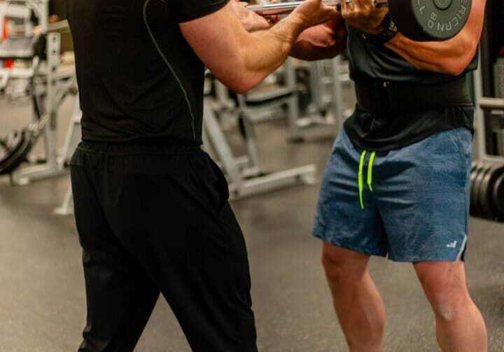 Personal trainer Joel Jenkins assisting client during intense barbell curl at failure in Oklahoma City gym